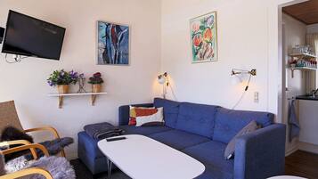 A living room with a blue sofa, a white coffee table, a TV mounted on the wall, and two wall-mounted lamps.