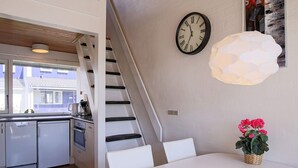 A modern kitchen with white cabinetry, a dining table with chairs, a staircase, a wall clock, and a hanging light fixture. - 5 Person Holiday Home in Vaeggerlose (Vaeggerlose)