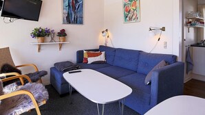 A modern living room with a blue sofa, a white coffee table, and a TV mounted on the wall. There are two shelves with decorative items and a lamp. - 5 Person Holiday Home in Vaeggerlose (Vaeggerlose)