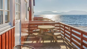 A wooden deck with a table and chairs, overlooking a body of water with mountains in the distance. - 6 Person Holiday Home in Brekstad (Orland)