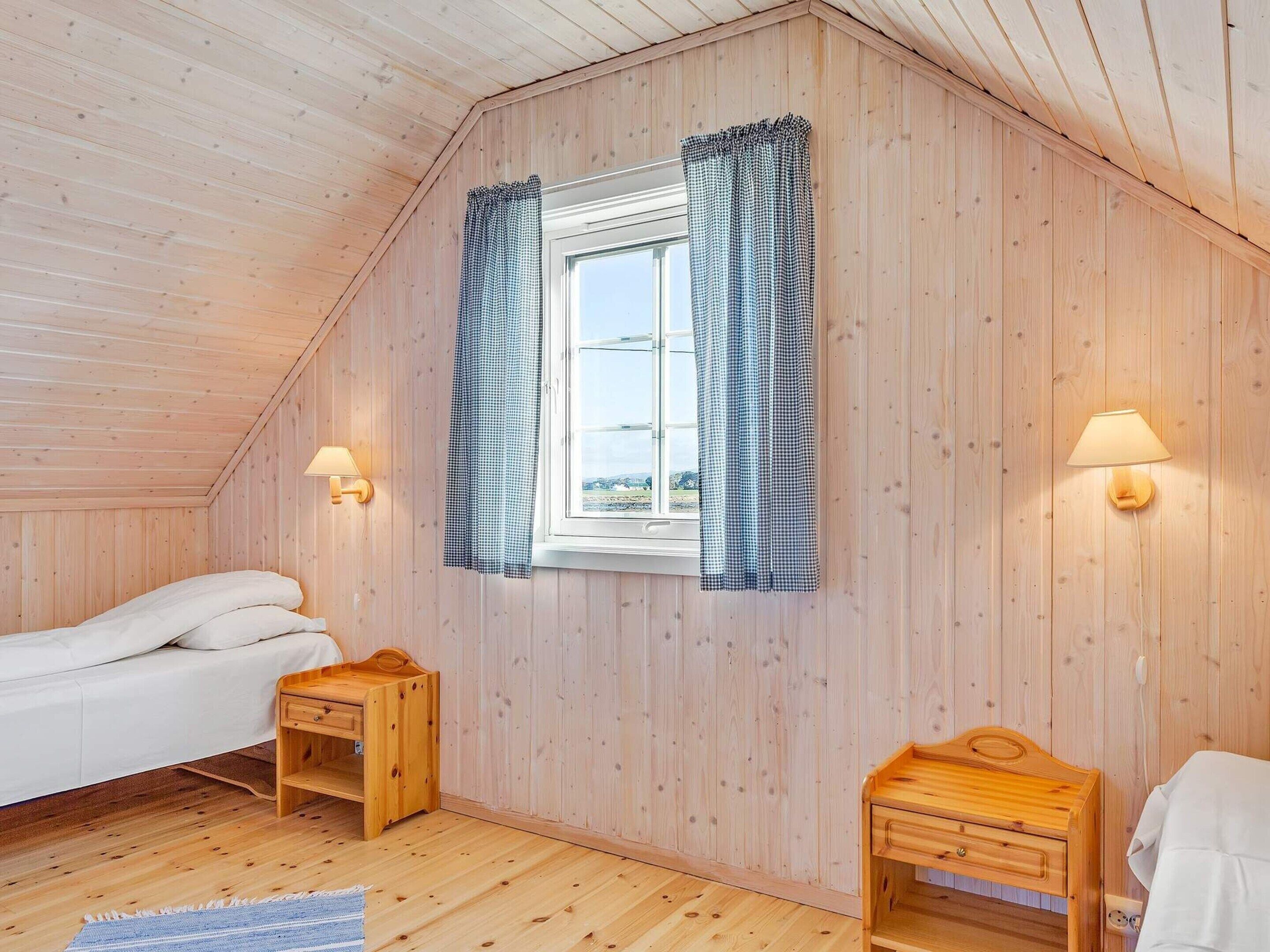 Een knus vertrek met houten wanden, een bed, een klein houten tafeltje, een nachtkastje en een raam met geruit gordijnen.