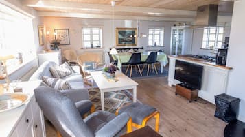 Amplia sala de estar con sofá, sillas, una mesa de comedor y una cocina con estufa y televisor.