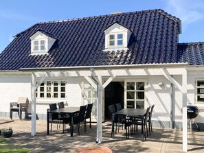 A house with a tiled roof, a covered patio with a table and chairs, and a barbecue grill. - 5 Person Holiday Home in Oster Assels (Øster Assels)