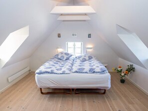 A bedroom with a sloped ceiling, a bed with patterned bedding, a small table with flowers, and a wall-mounted light fixture. - 5 Person Holiday Home in Oster Assels (Øster Assels)