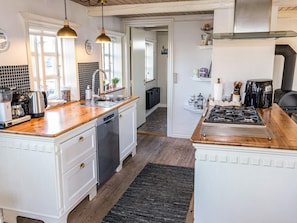 A modern kitchen with white cabinetry, a wooden countertop, a built-in dishwasher, a stove, and a coffee maker.