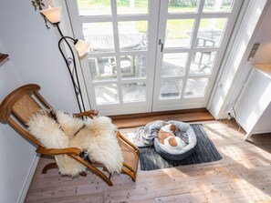 Um quarto com uma cadeira de madeira, um tapete macio, uma cama de cachorro e um abajur.