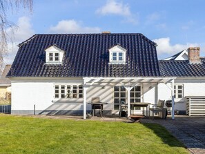 Een tweelaags huis met een donker betegeld dak, witte buitenmuren en een overdekte patio met buitenmeubilair.