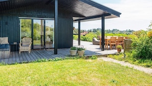 A modern house with a wooden deck, a glass door leading to a patio, and a view of the countryside. - 4 Star Holiday Home in Ebeltoft (Ebeltoft)