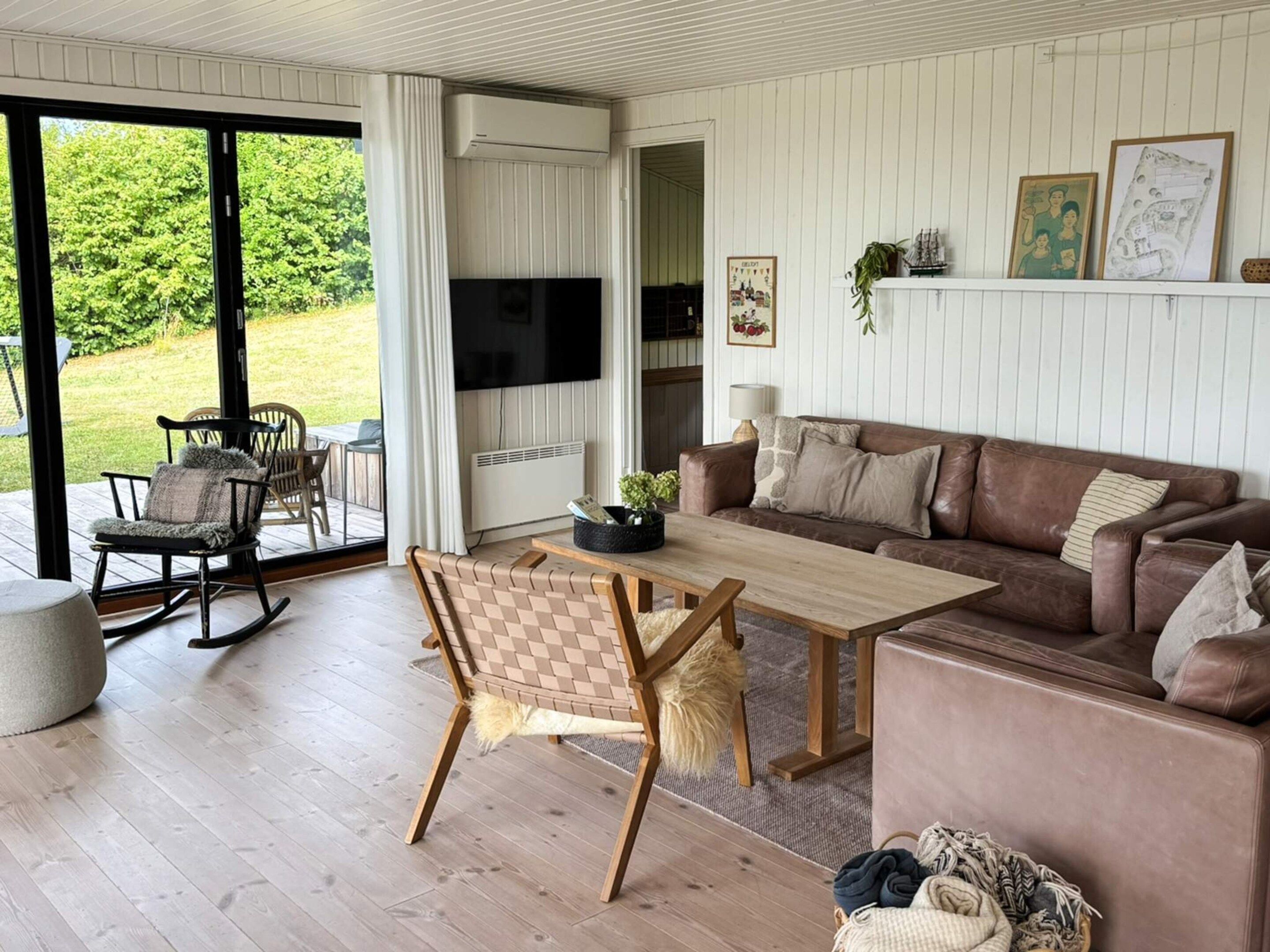 Ein modernes Wohnzimmer mit Couchtisch aus Holz, einer braunen Ledersofa und einem Essbereich mit Schaukelstuhl und Tisch.