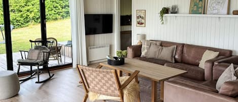 Een moderne woonkamer met een houten salontafel, een bruine leren bank en een eethoek met een schommelstoel en een tafel.