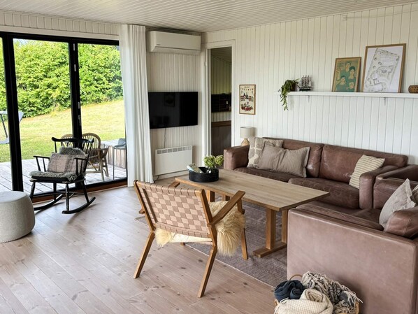 A modern living room with a wooden coffee table, a brown leather sofa, and a dining area with a rocking chair and a table. - 4 Star Holiday Home in Ebeltoft (Ebeltoft)