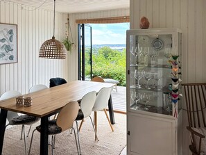 A dining area with a wooden table, white chairs, and a glass cabinet with wine glasses. - 4 Star Holiday Home in Ebeltoft (Ebeltoft)