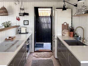 A modern kitchen with a black door, stainless steel appliances, and a wooden shelf. - 4 Star Holiday Home in Ebeltoft (Ebeltoft)