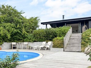 A pool area with a wooden deck, lounge chairs, and a staircase leading to a modern building. - 4 Star Holiday Home in Ebeltoft (Ebeltoft)