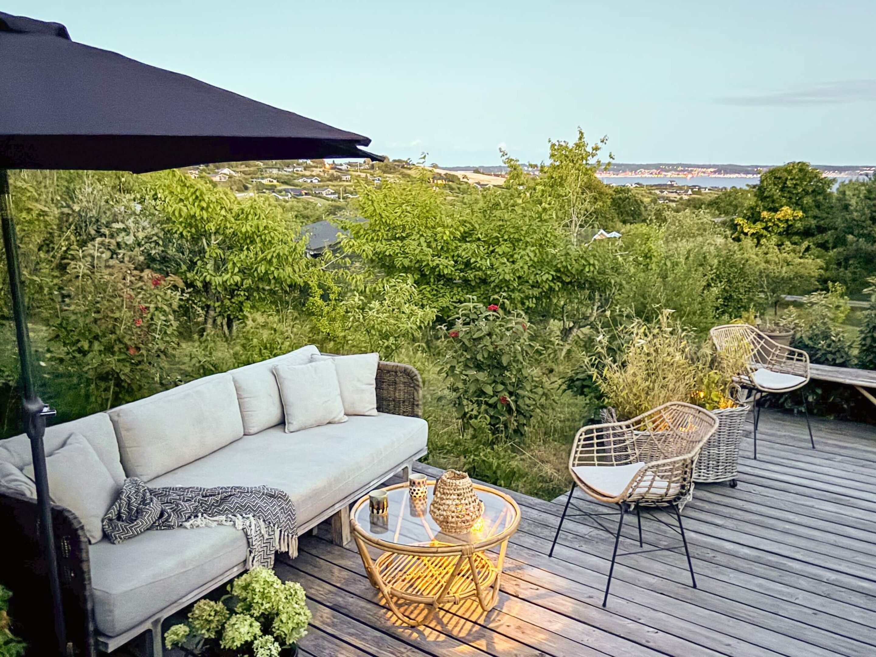 En terrasse med sofa, stole og et bord, med udsigt over et frodigt landskab.