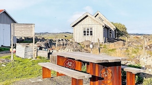 A rustic wooden building with a slanted roof, a bench with a bicycle emblem, and a signboard.