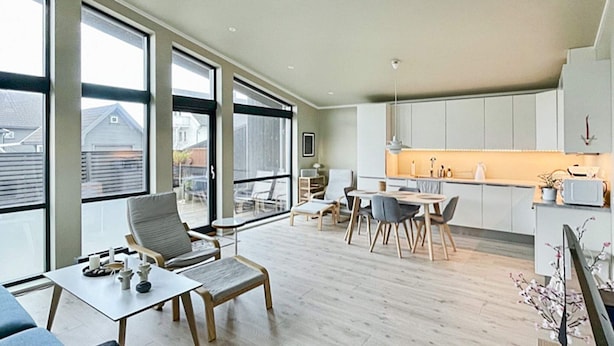 A modern kitchen with white cabinets, a dining area with a table and chairs, and large windows offering a view of the outside.