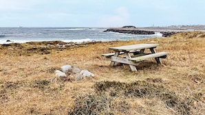 A picnic table in a grassy area with a view of the ocean and a rocky shoreline.