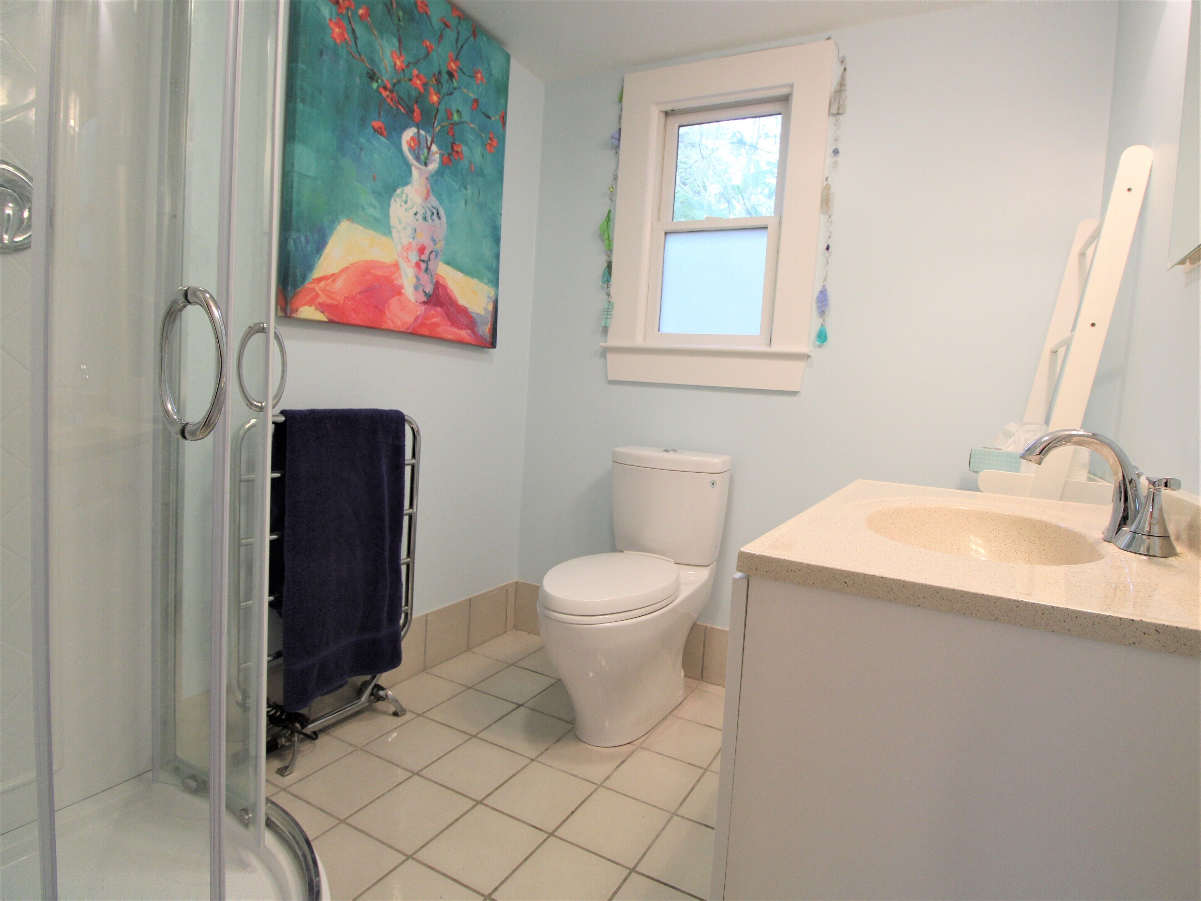 Un bagno con cabina doccia in vetro, un WC bianco, un lavandino con specchio e un quadro sopra il water.