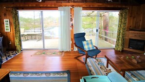 Un intérieur en bois avec un fauteuil à bascule, une cheminée et une vue dégagée grâce à de grandes portes vitrées.