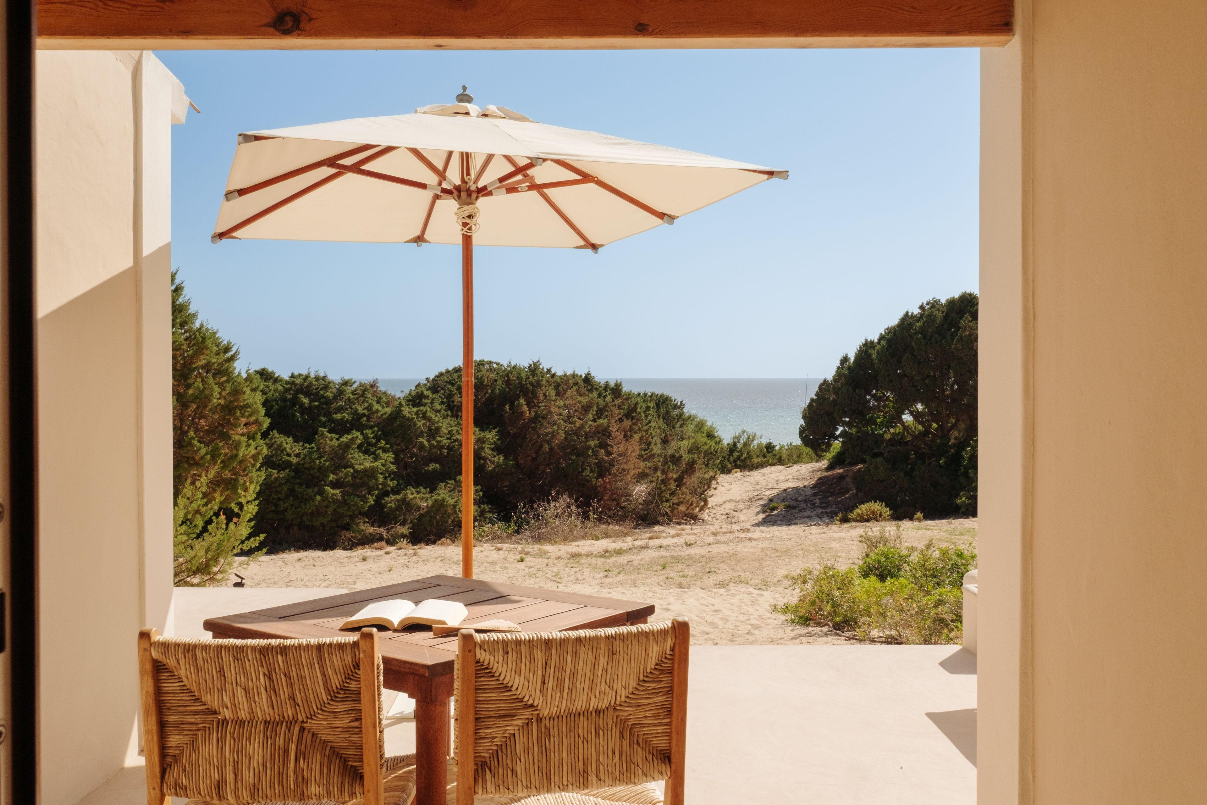 Et udendørs opholdsområde med et bord, stole og en parasol, samt udsigt til strand og hav.