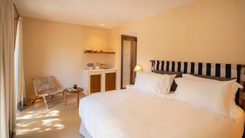 A hotel room with a large bed, a small desk with a chair, a nightstand, and a window with curtains.