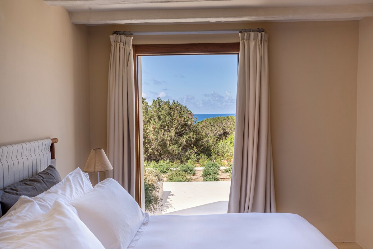 Une chambre d’hôtel avec un lit, une lampe et une vue sur la mer, visible à travers de grandes fenêtres.