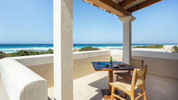 A balcony with a wooden table and chairs, overlooking a beach and ocean. - Dunas de Formentera Hotel (Formentera)