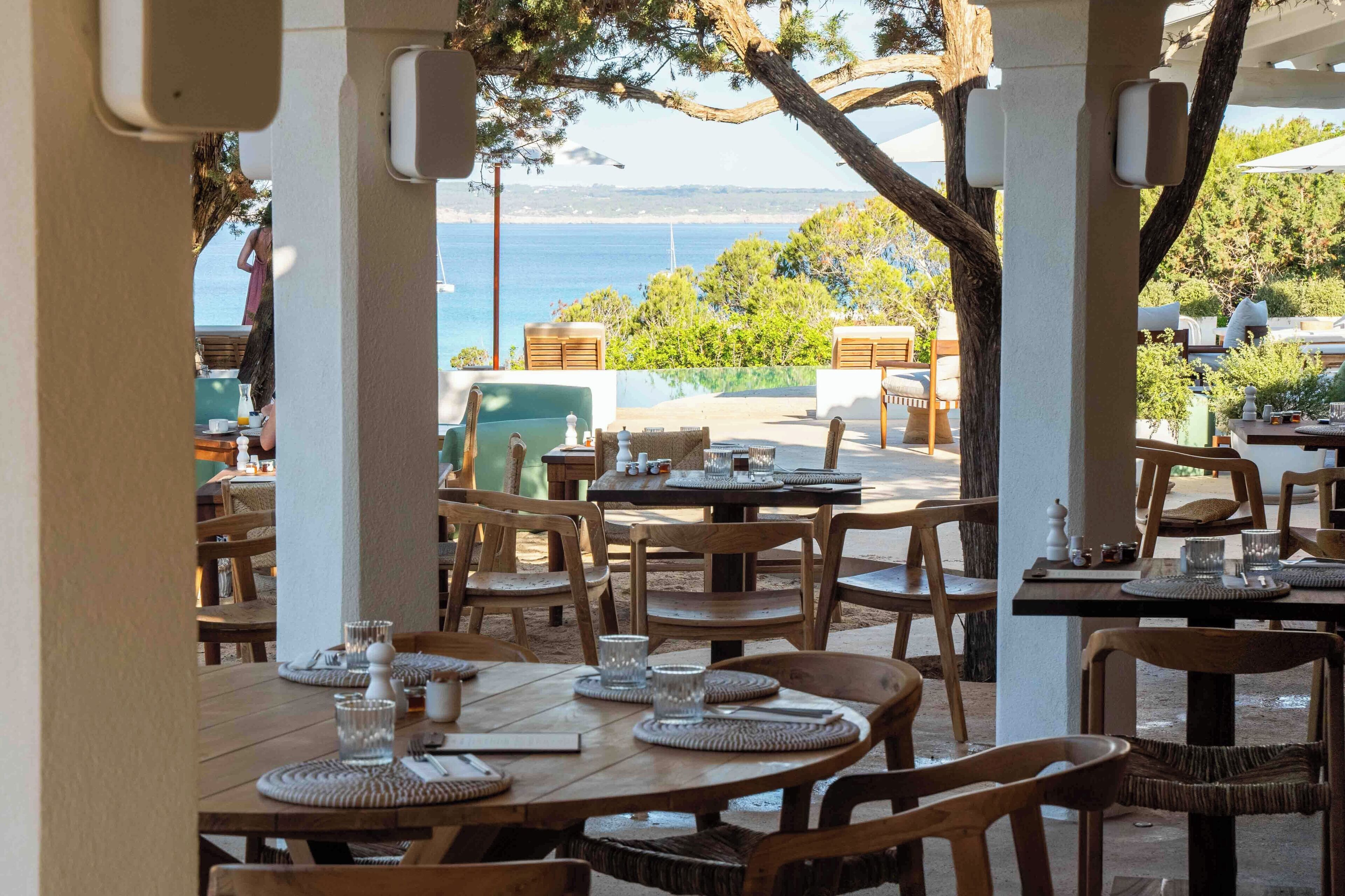 Un área de comedor al aire libre con mesas y sillas, con vistas a un paisaje marino.