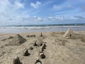 En sandstrand med flera sandskulpturer och en pyramidformad konstruktion.