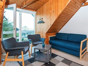 A room with a wooden ceiling, a blue sofa, two armchairs, a small table, and a view through a glass door. - 5 Person Holiday Home in Romo (Rømø)