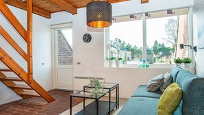 A modern living room with a wooden staircase, a black coffee table, a green sofa, and a view of the outdoors through large windows.