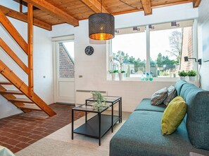 A modern living room with a wooden staircase, a black coffee table, a green sofa, and a view of the outdoors through large windows.