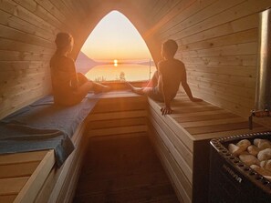 Et sauna-rum med trævægge og bænke, udsigt til solnedgang og et sauna-bad med et synligt brandnavn.