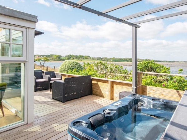 A deck with outdoor seating and a hot tub overlooking a body of water.