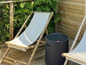 A wooden deck with a bamboo chair and a wicker trash bin.