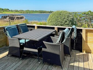 Une terrasse extérieure avec une table et des chaises, donnant sur une étendue d’eau et une zone verdoyante.