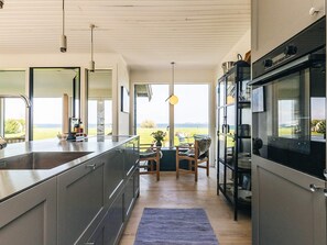 Une cuisine moderne dotée d’un grand îlot central, d’appareils électroménagers intégrés et offrant une vue sur l’extérieur.