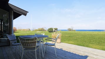 Eine Terrasse im Freien mit Tisch und Stühlen, mit Blick auf eine Wiese und das Meer.