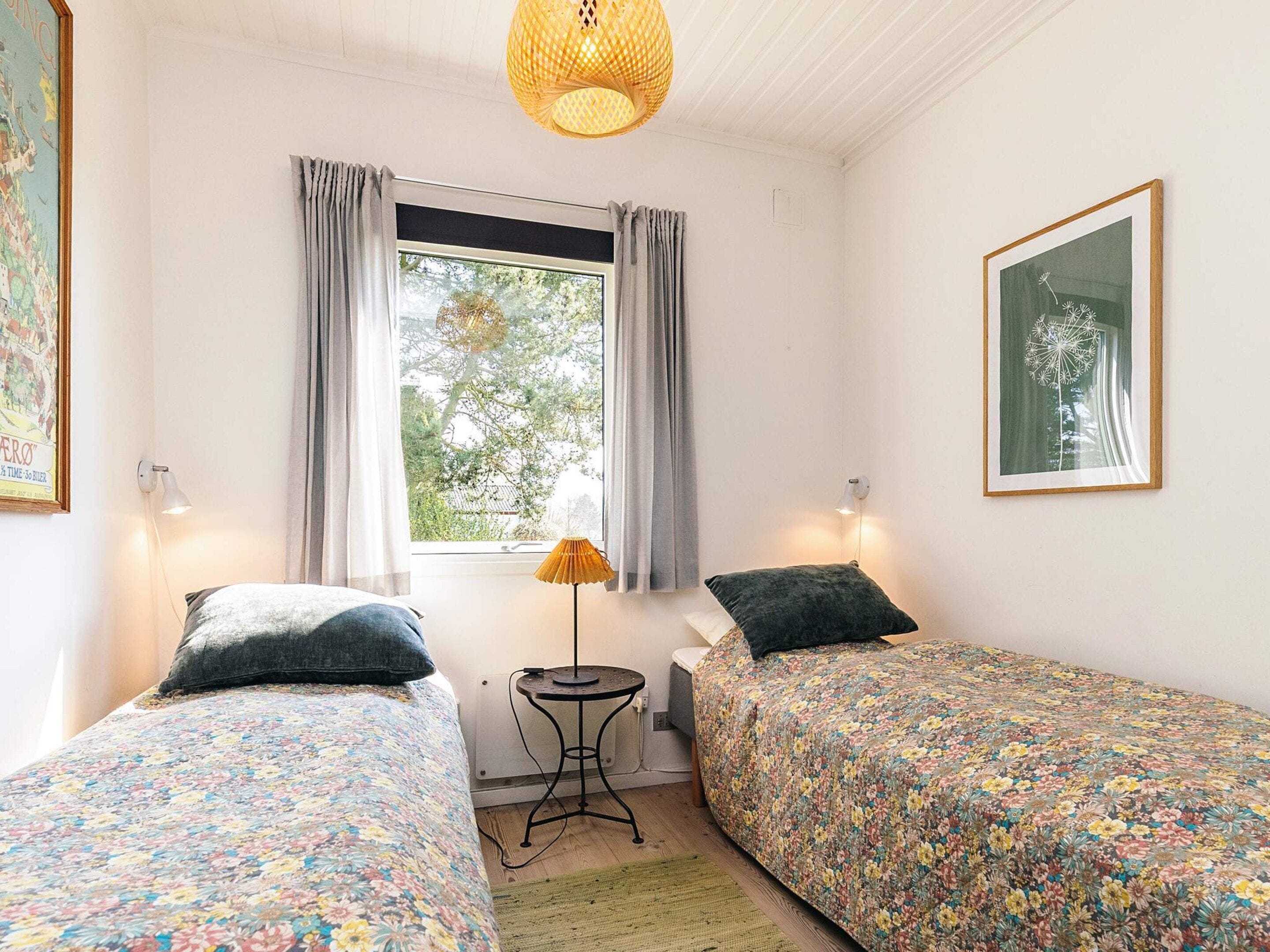 Un dormitorio con dos camas individuales, una ventana con cortinas, una lámpara de pie y un cuadro en la pared.