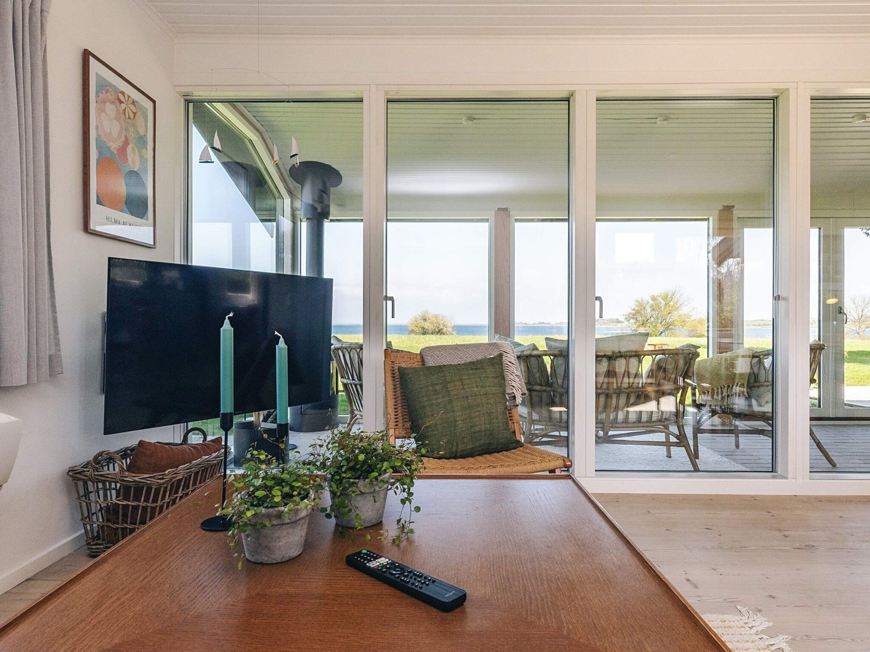 A living room with a large TV, potted plants, and a remote control on a wooden table.
