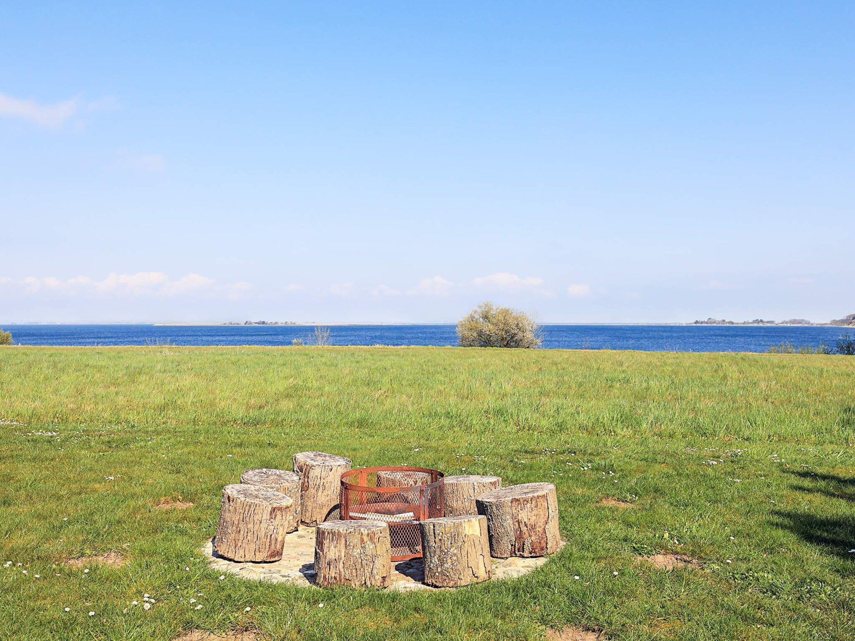 A grassy field with a circular arrangement of wooden stumps and a metal fence in the center, overlooking a body of water.