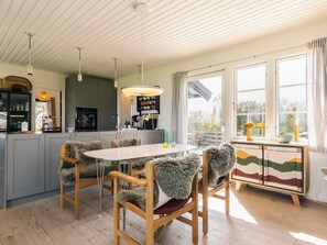 A modern kitchen with grey cabinets, a central island, and a dining area with a round table and chairs.