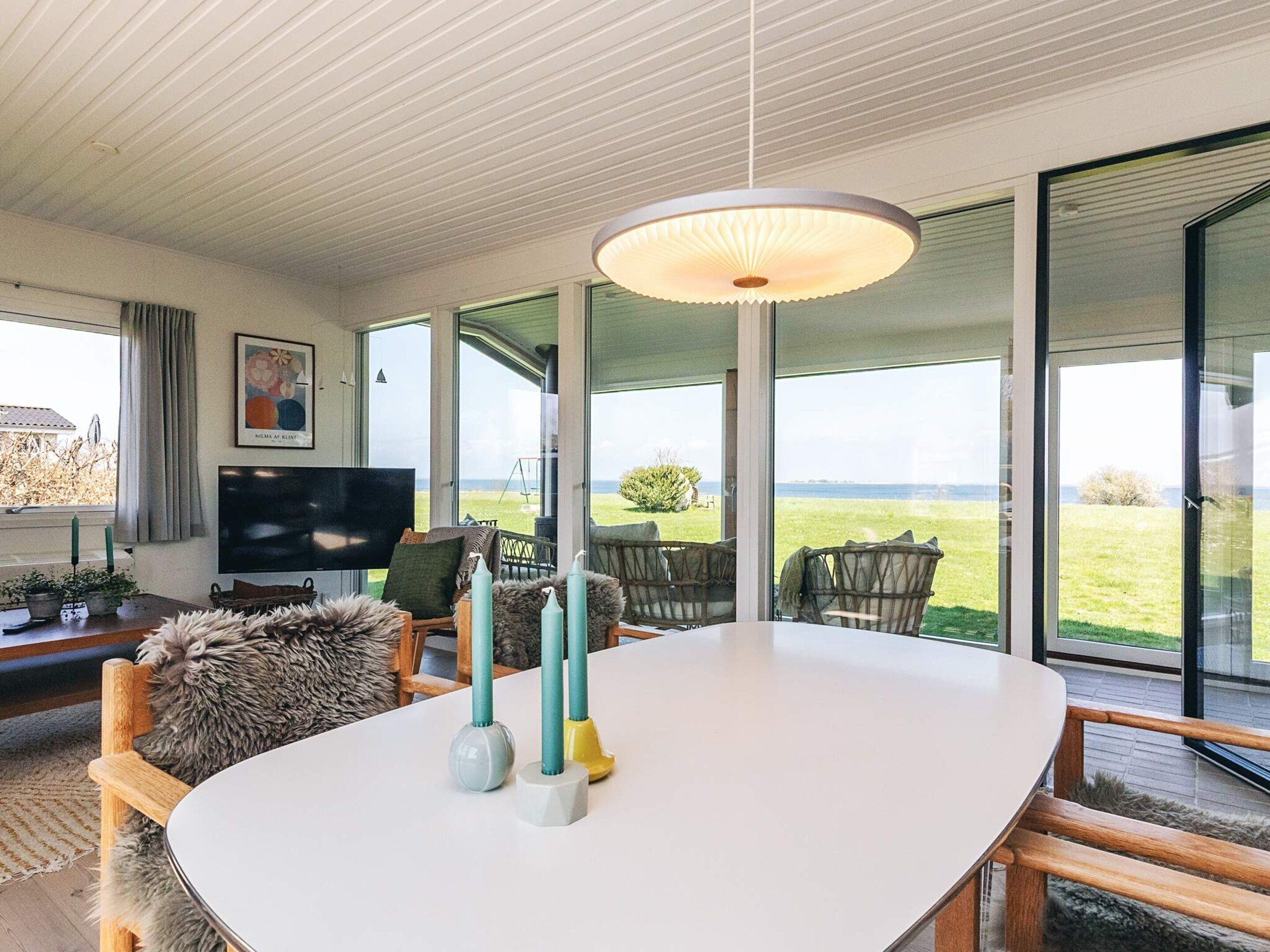 Ein modernes Wohnzimmer mit einem großen weißen Tisch, bequemen Sitzgelegenheiten, einem Flachbildfernseher und Blick ins Freie.