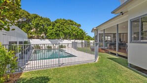 Una casa moderna con piscina, patio cubierto y césped cuidado.
