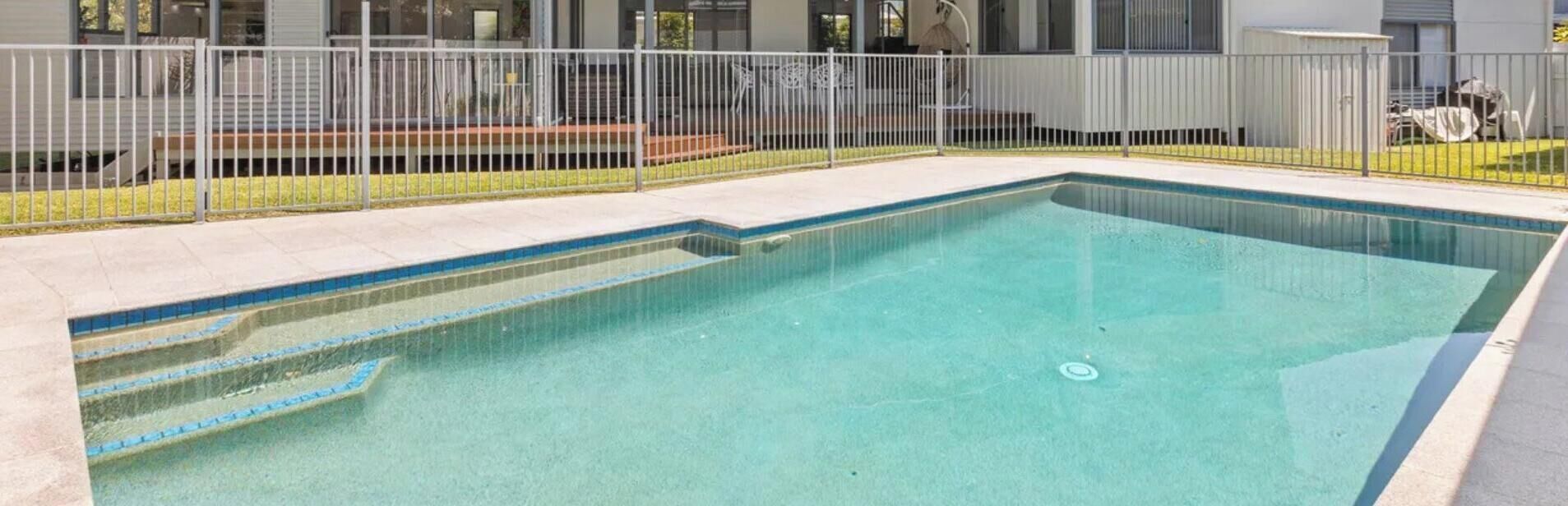 A rectangular swimming pool with a metal fence and steps leading into it.