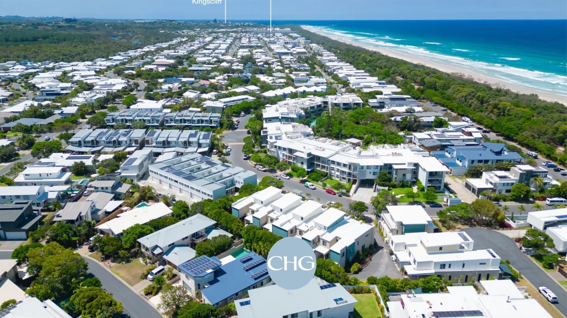 An aerial view of a coastal residential area with modern houses, a beach, and a clear sky.