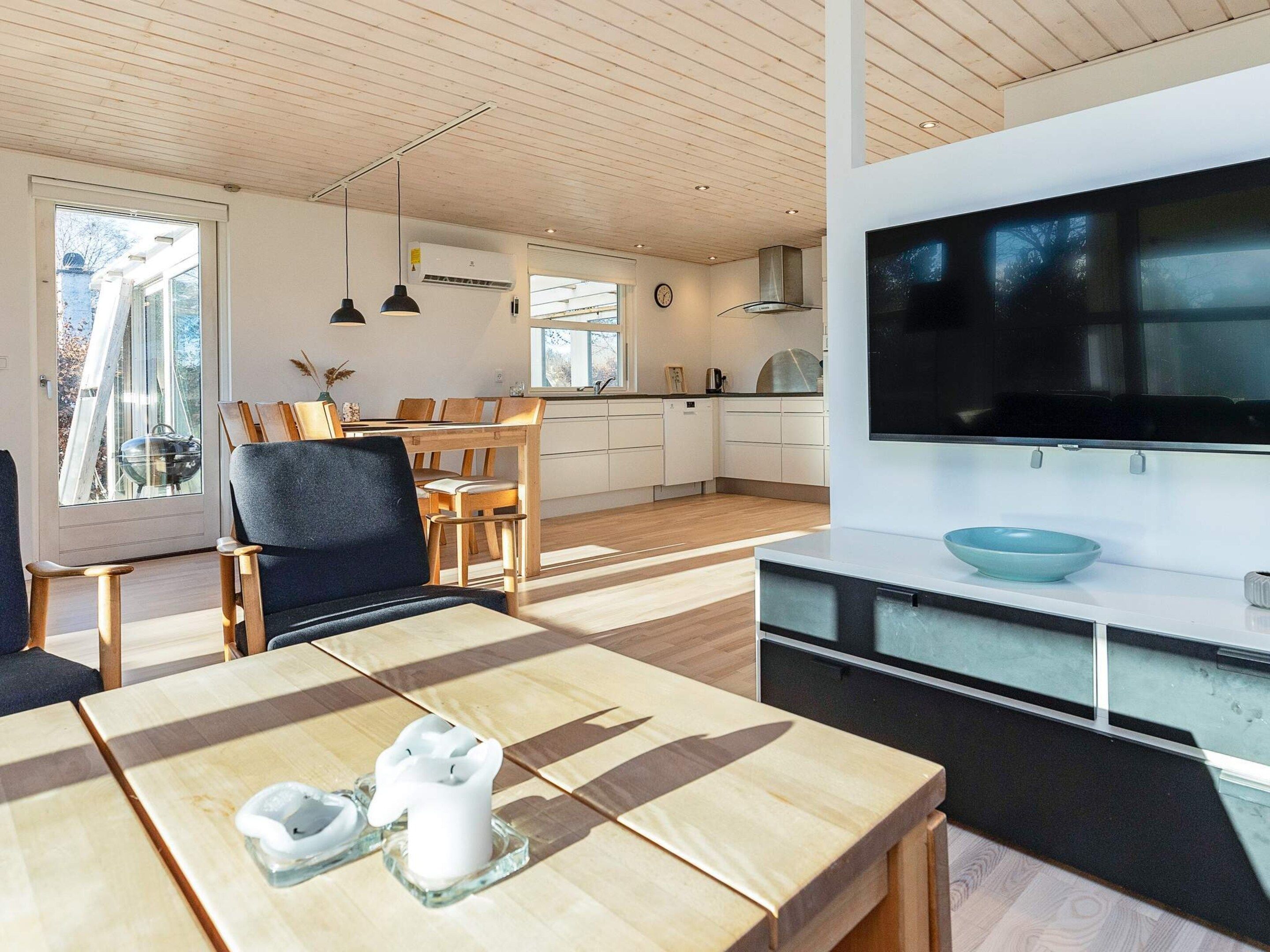 Una cocina moderna con televisor grande, mesa de comedor de madera y vistas al exterior.
