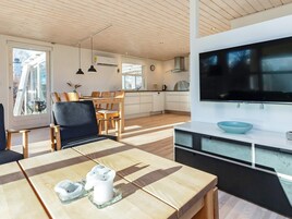 A modern kitchen with a large TV, wooden dining table, and a view of the outdoors.