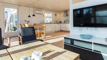A modern kitchen with a large TV, wooden dining table, and a view of the outdoors.